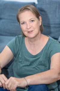 Gudrun Kirchert in grünem Shirt vor blauem Sofa, lächelnd