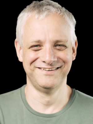 Mann mit grünem Shirt, lächelnd vor schwarzem Hintergrund